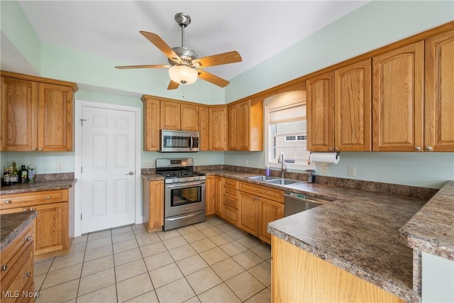 kitchen featuring dark countertops, appliances with stainless steel finishes, brown cabinetry, a ceiling fan, and a sink