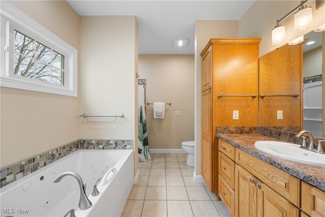 bathroom with tile patterned flooring, toilet, vanity, baseboards, and a tub with jets