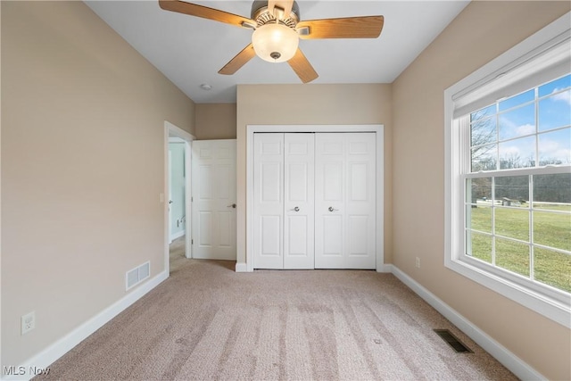 unfurnished bedroom featuring baseboards, multiple windows, visible vents, and light colored carpet