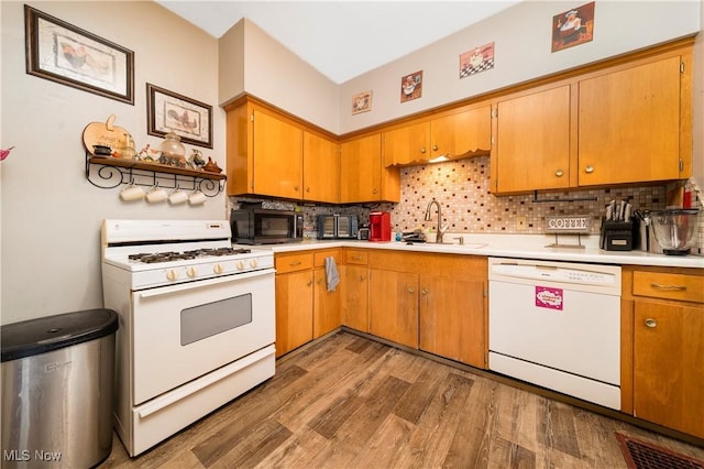 kitchen featuring white appliances, brown cabinets, wood finished floors, light countertops, and a sink