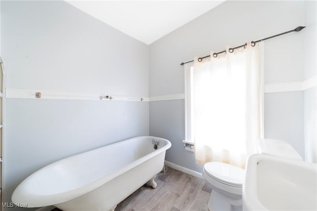 bathroom with a freestanding bath, wood finished floors, toilet, and baseboards