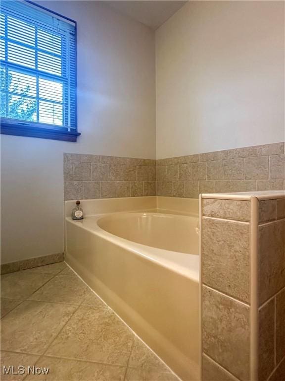 full bath featuring tile patterned flooring, baseboards, and a bath