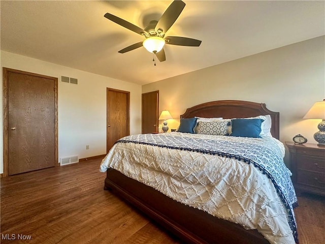 bedroom with multiple closets, dark wood-style flooring, visible vents, and ceiling fan