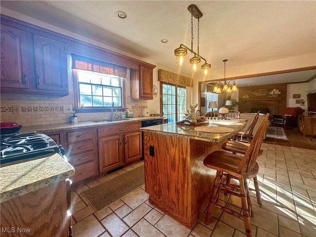 kitchen featuring a breakfast bar, a center island, hanging light fixtures, brown cabinetry, and a sink