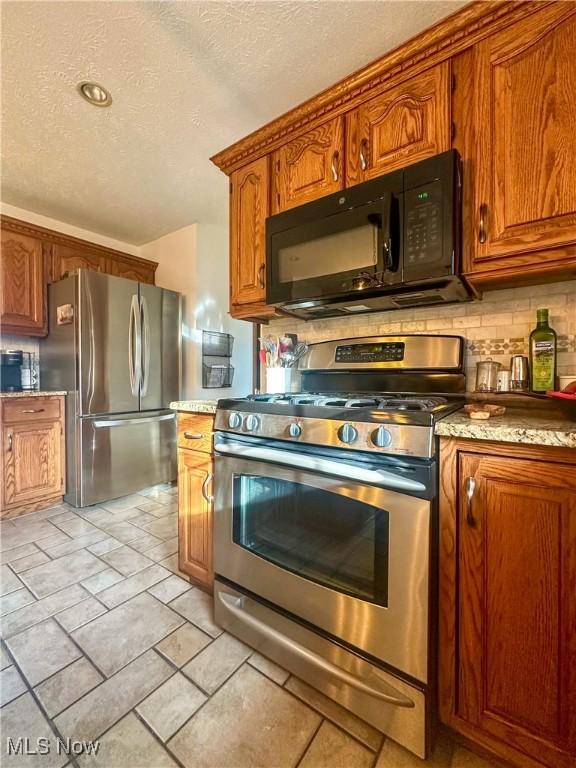 kitchen featuring brown cabinetry, decorative backsplash, appliances with stainless steel finishes, light countertops, and a textured ceiling