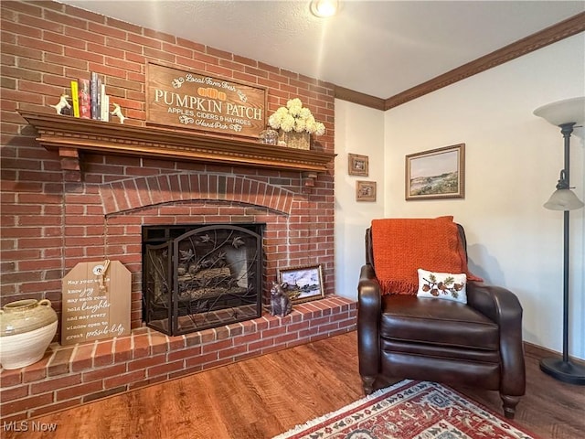 living area featuring a brick fireplace, crown molding, baseboards, and wood finished floors