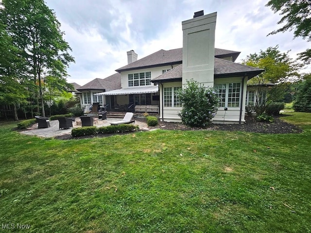 rear view of house with a chimney, a lawn, and a patio area