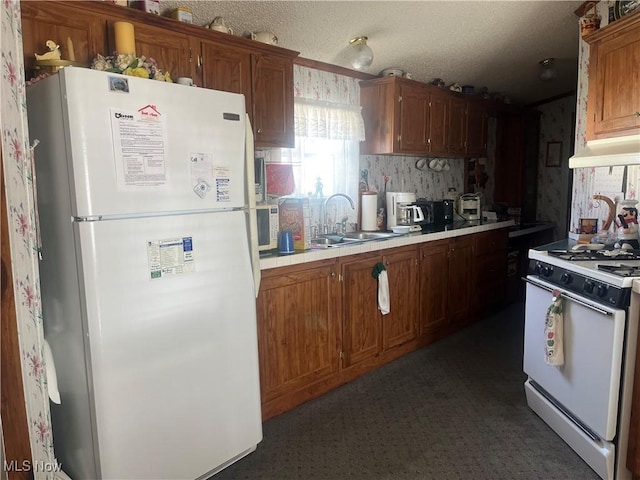 kitchen with under cabinet range hood, white appliances, a sink, tile counters, and brown cabinets