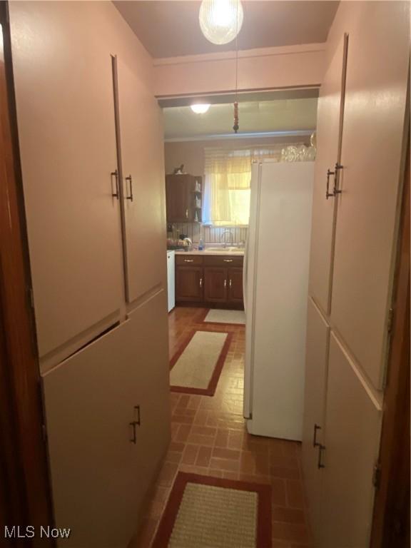 hallway with brick patterned floor, a sink, and crown molding