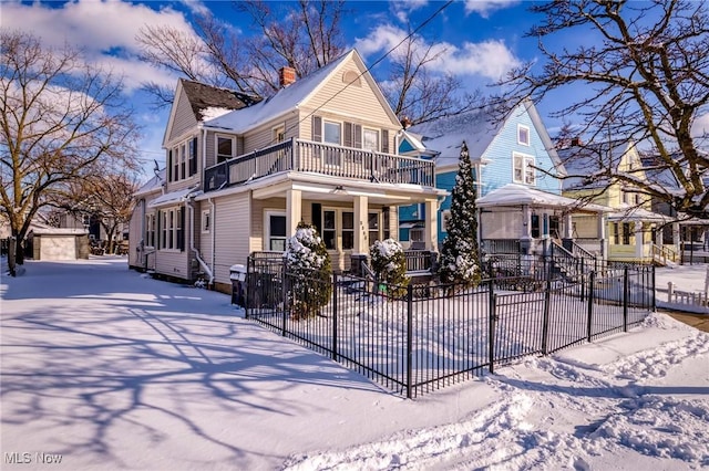 view of front of home featuring driveway, a balcony, a fenced front yard, a chimney, and a porch