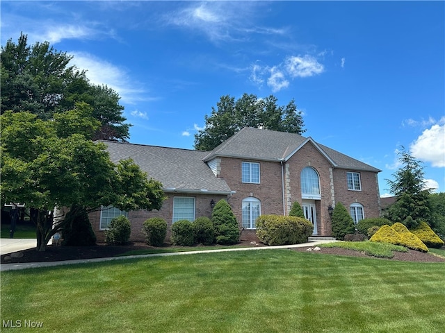 colonial inspired home featuring a front yard, brick siding, and roof with shingles