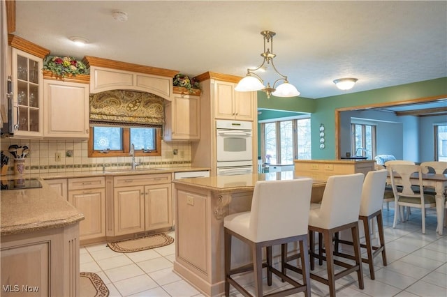 kitchen with white double oven, a kitchen island, a sink, a kitchen bar, and backsplash