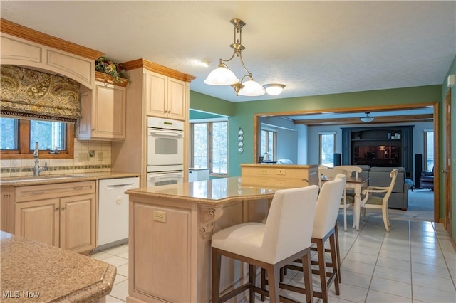 kitchen with light tile patterned floors, white appliances, a breakfast bar, a sink, and decorative backsplash