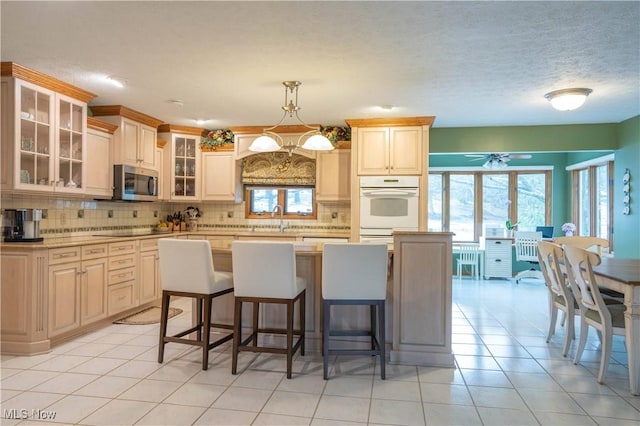 kitchen featuring tasteful backsplash, light countertops, stainless steel microwave, a sink, and oven