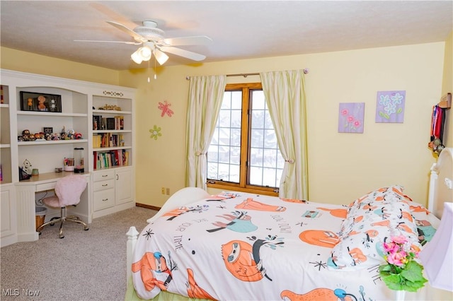 carpeted bedroom with built in desk, a ceiling fan, and baseboards