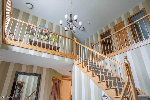 stairway with a high ceiling, an inviting chandelier, and wallpapered walls