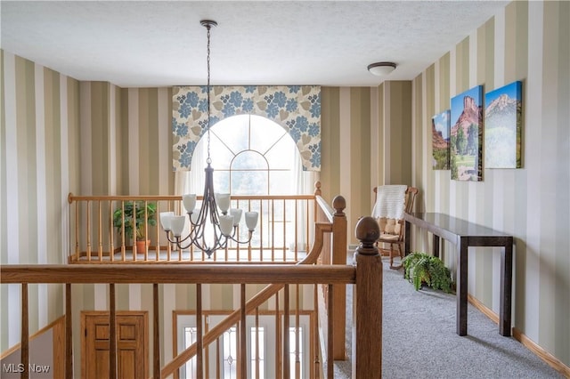 hallway featuring a textured ceiling, carpet flooring, baseboards, wallpapered walls, and an inviting chandelier