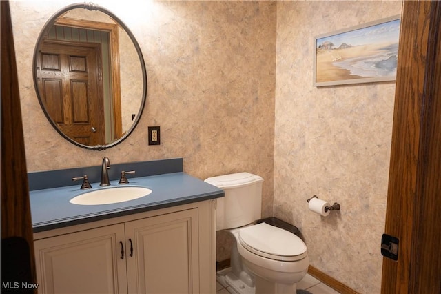 half bath with baseboards, vanity, toilet, and wallpapered walls