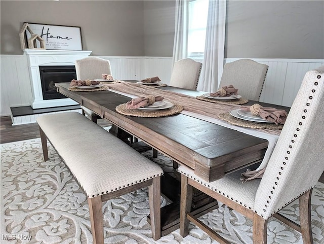 dining room with wainscoting, a fireplace with raised hearth, and light wood finished floors