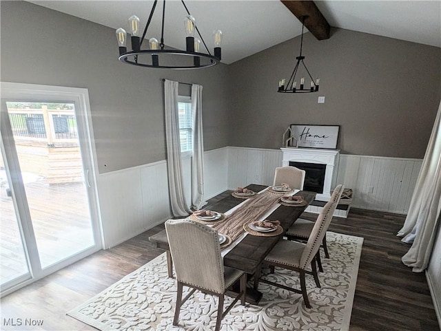 dining space featuring vaulted ceiling with beams, a wainscoted wall, a fireplace, wood finished floors, and an inviting chandelier