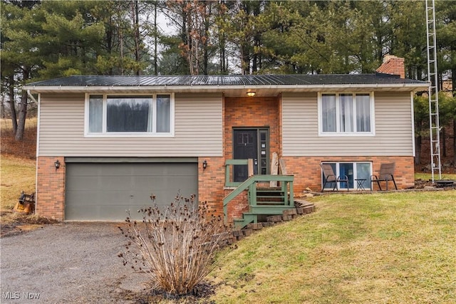 bi-level home with an attached garage, metal roof, a front lawn, and brick siding