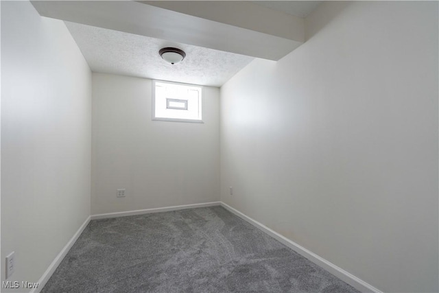 basement featuring baseboards, dark carpet, and a textured ceiling