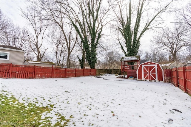 snowy yard featuring an outbuilding, a fenced backyard, and a storage shed