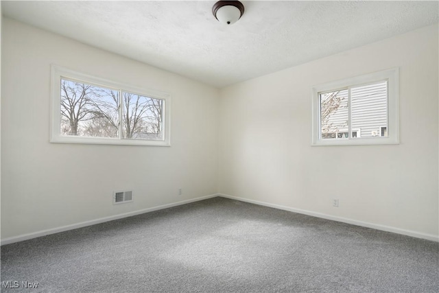 carpeted spare room featuring a healthy amount of sunlight, visible vents, and baseboards