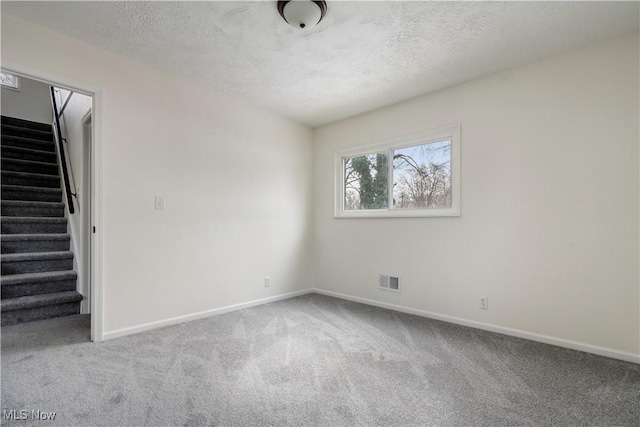 carpeted empty room with baseboards, stairs, visible vents, and a textured ceiling