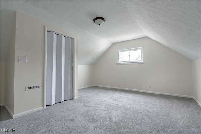 bonus room with a textured ceiling, light carpet, lofted ceiling, and visible vents