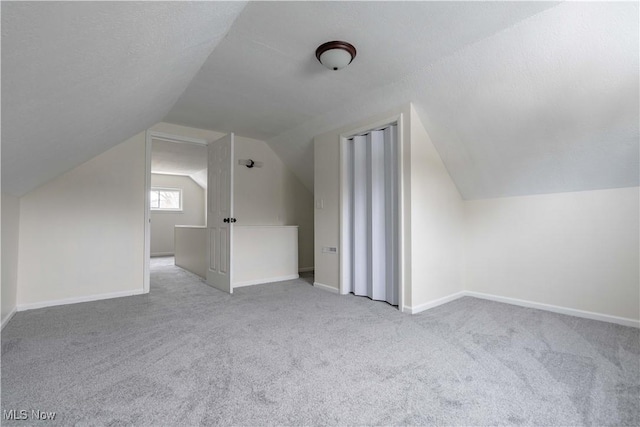 additional living space with lofted ceiling, light carpet, and baseboards