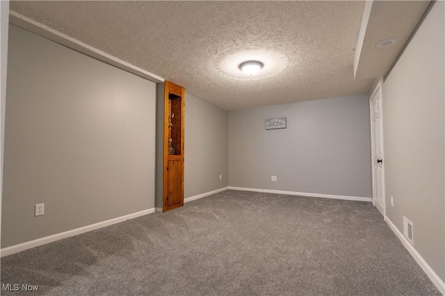 empty room with baseboards, visible vents, a textured ceiling, and carpet flooring