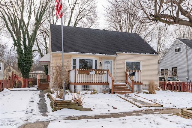 cape cod home featuring a shingled roof, fence, and a deck