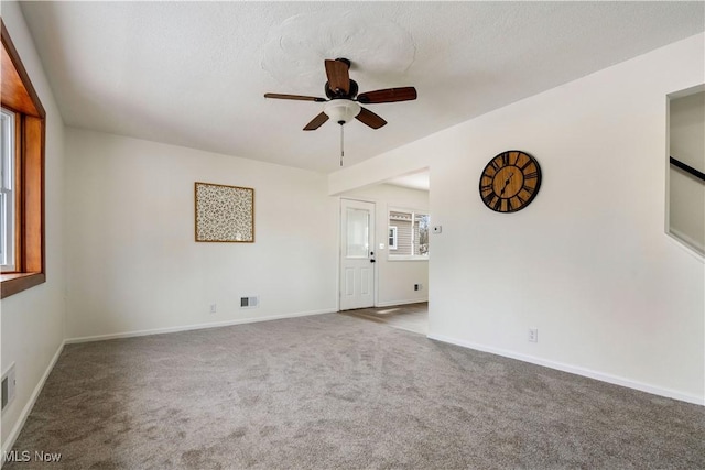 empty room with ceiling fan, a textured ceiling, carpet floors, visible vents, and baseboards