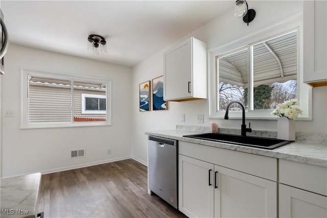 kitchen with light wood finished floors, light stone counters, stainless steel dishwasher, white cabinetry, and a sink