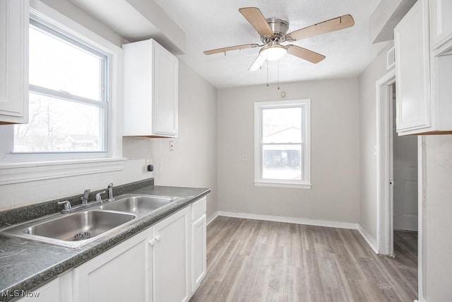 kitchen with light wood-style floors, dark countertops, white cabinetry, and a sink