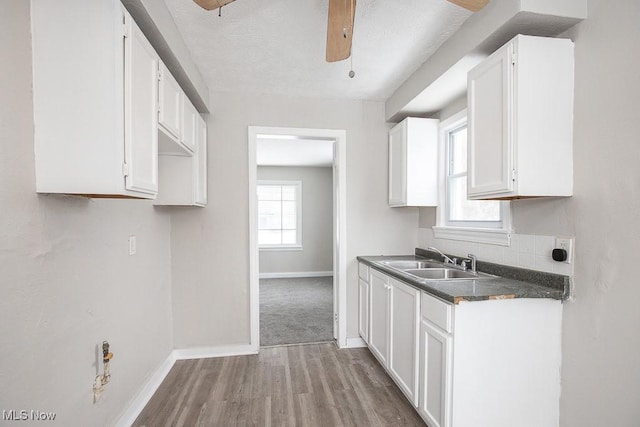 kitchen featuring dark countertops, light wood-style flooring, white cabinetry, a sink, and baseboards