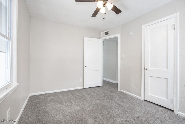 unfurnished bedroom featuring carpet, multiple windows, visible vents, and baseboards