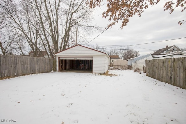 snow covered garage featuring a detached garage and fence