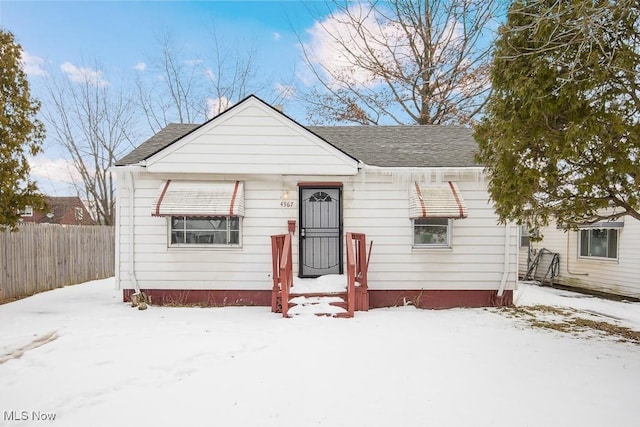 bungalow-style house with a shingled roof and fence