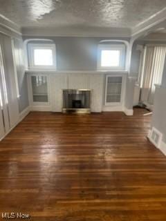 unfurnished living room with a textured ceiling, dark wood-style flooring, a glass covered fireplace, and visible vents