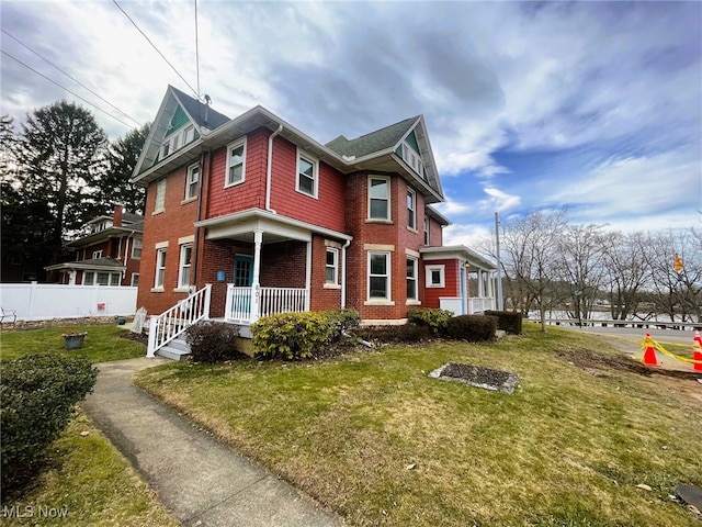 view of front of home with a front yard, fence, a porch, and brick siding