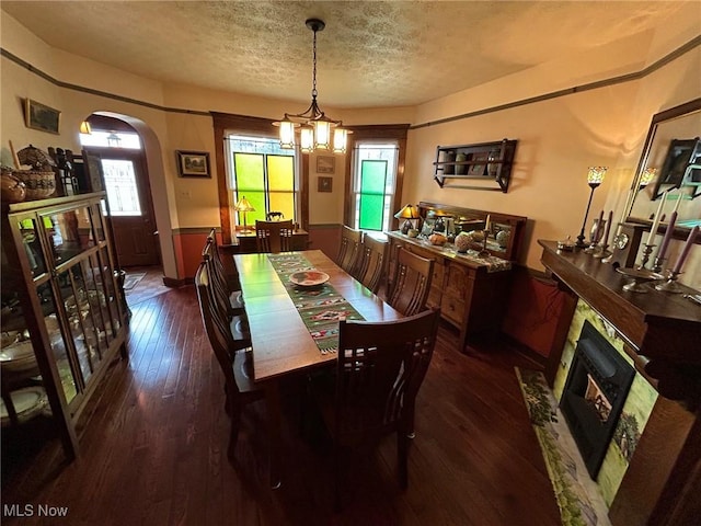 dining space featuring arched walkways, dark wood-style flooring, a wainscoted wall, a premium fireplace, and a textured ceiling