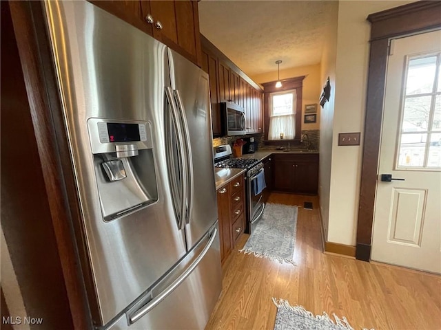 kitchen featuring stainless steel appliances, visible vents, light wood-style floors, hanging light fixtures, and dark countertops