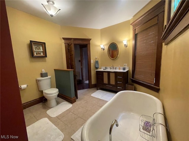 bathroom with tile patterned flooring, a freestanding tub, toilet, vanity, and baseboards