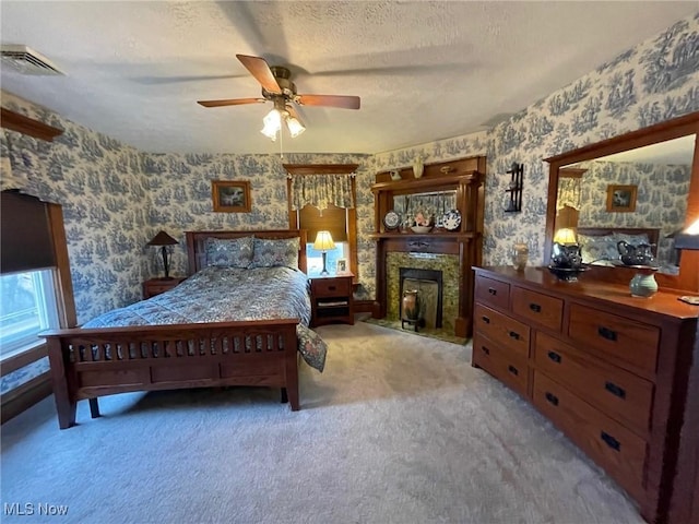 carpeted bedroom featuring a textured ceiling, a fireplace, a ceiling fan, visible vents, and wallpapered walls