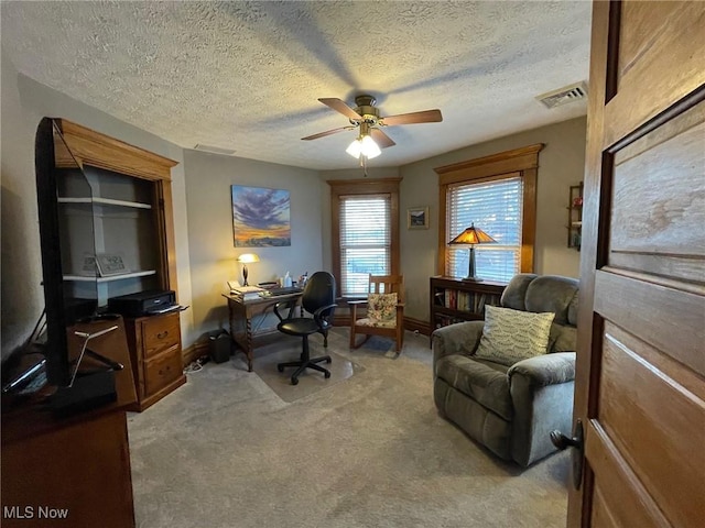 home office with light carpet, a textured ceiling, visible vents, and a ceiling fan