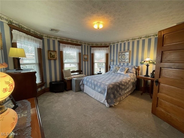 bedroom featuring light carpet, visible vents, a textured ceiling, and wallpapered walls