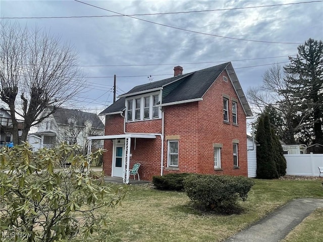 rear view of house with a chimney, fence, a lawn, and brick siding