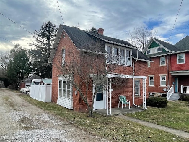 back of property featuring a shingled roof, brick siding, fence, and a chimney